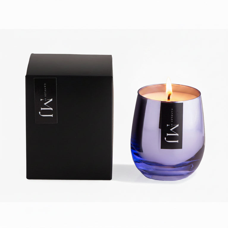 A purple glass candle with a black lid, next to its black packaging box with a logo on it, on a white background.