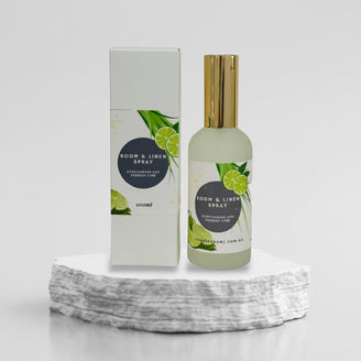 A bottle of room and linen spray with a label that reads 'Lemongrass & Persian Lime'. The bottle is tinted green with a white label and gold accents on the cap.