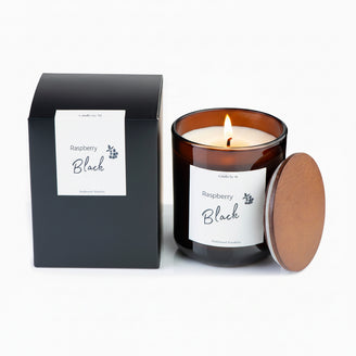 A black candle with a clear label that reads 'Black Raspberry' in a brown wax packaging with a lid.