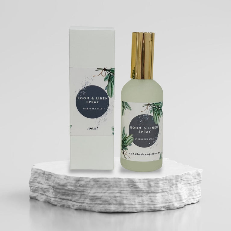A room and linen spray bottle with a white label and a gold cap, placed on a textured surface.