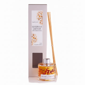 A SANDALWOOD & PATCHOLI 200ML Botanical Reed Diffuser with a glass bottle and several reeds placed in front, set against a white background.