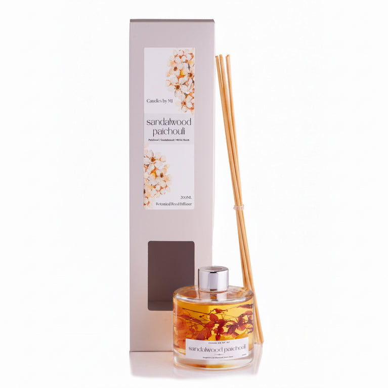 A SANDALWOOD & PATCHOLI 200ML Botanical Reed Diffuser with a glass bottle and several reeds placed in front, set against a white background.