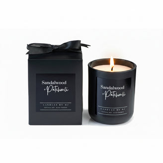 A black candle with a label reading 'Sandalwood & Patchouli' alongside a black box with the same label.